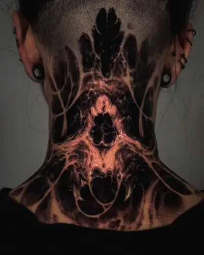 Blackwork neck tattoo by Andrew Stopay: a symmetrical bio-horror skull with fangs and organic, vein-like textures across the back of the neck