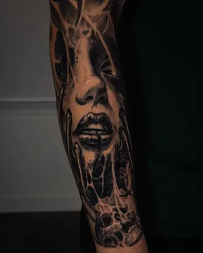 Black and grey forearm tattoo by Andrew Stopay: a surreal female face with dripping lips, skeletal fingers and web-like textures
