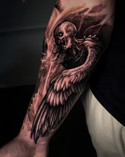 Black and grey forearm tattoo by Andrew Stopay: a decaying skeletal figure with a large feathered wing