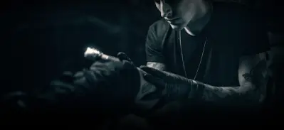Andrew Stopay at work with a tattoo machine in a dark studio