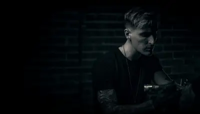 Andrew Stopay tattooing in front of a dark brick wall